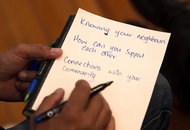 A hand holds a notepad with handwritten notes on community support and connections, featuring blue ink and a green pen.